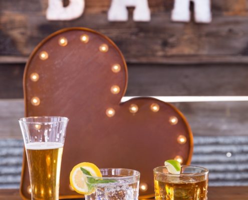 Beer Pilsner & Carat Rocks Glasses On Whiskey Barrel Bar With Barnwood Decor Wall & Bar Sign